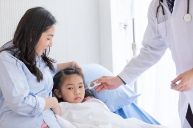 Pediyatrist doktor çocuğun kulağının ısısını ölçüyor ve annesi de hastanede yanında..