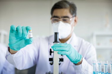 Koruyucu eldivenler ve iş kıyafetlerinde uzman olarak bir tepsi COVID-19 aşı şişesi düzenliyorum. Profesyonel, COVID-19 aşısı üzerinde laboratuvarda araştırma yapıyor..