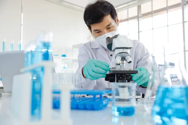 Young Asia Male Scientist Looking Lens Microscope While Being Seated Stock Photo