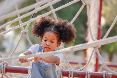 Küçük Afrikalı kıvırcık saçlı kız bahar ya da yaz sezonunda parkta oynuyor. İp ekipmanına tırmanmayı seviyorlar..