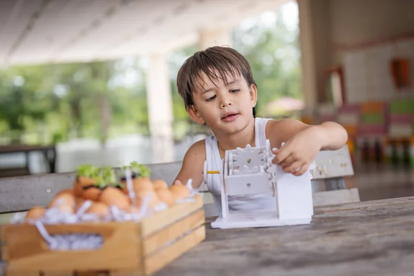 A boy and pay attention to learning the simulation mechanism robot model wooden on table at home.