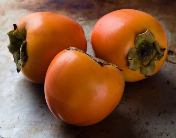 Persimmons on steel plate — Stock Photo, Image