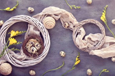 Paskalya düzlüğü, kuş yuvasında bıldırcın yumurtaları, keten tekstil ve çevresi ile koyu bir zemin üzerinde uzanıyordu. Koyu arkaplanda sarı frezya çiçekleri ve rattan çelengi. Sıfır doğal Paskalya süslemesi.