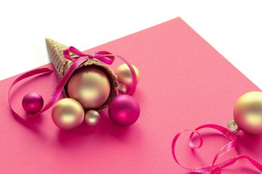 Pembe kağıt üzerinde Xmas altın topları, yıldızları ve kurdeleleri olan altın waffle dondurma külahı. Mutlu Noeller mesajı at. Xmas dekorasyonları, beyaz arkaplanda izole edilmiş düzenleme.