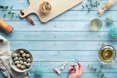 Mavi ahşap masada sıfır atık Paskalya arkaplanı. Bıldırcın yumurtası, doğal bahar süslemeleri, dallar ve okaliptüs. Cam çaydanlıkta yeşil çay. Paskalya tavşanı, tahta oyuncak..