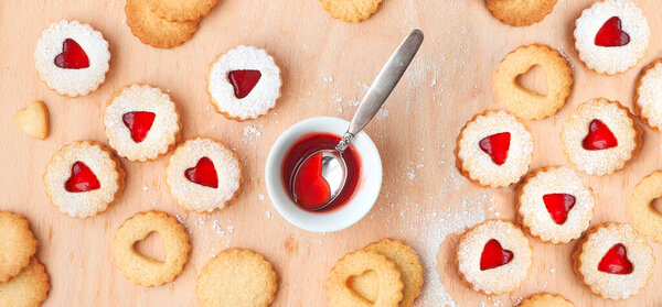 Top view of traditional Christmas Linzer cookies filled with strawberry jam on wooden board. Panoramic composition with traditional Austrian filled biscuits.