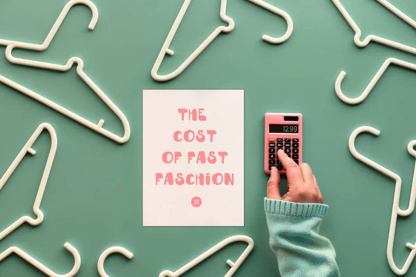 ファストファッションのコスト 白いプラスチック製のハンガー 計算機とテキスト付きの紙で手 パステルグリーンのミントの背景に創造的なフラットレイアウト — ストック写真