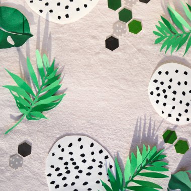 Moda düz yatış, dekoratif kağıt elementleri ile üst görünüm, beyaz tekstil arka planı yeşil. Egzotik yapraklar, benekli soyut şekiller ve kağıt altıgenler..