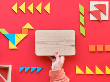 2 Nisan Dünya Otizm Günü için yaratıcı tasarım. Tangram elementleri kırmızı arkaplanda piktograma dağıldı ve düzenlendi. Metin alanı ve kopyalama alanı olan ahşap tahtayı elle tutun.