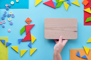 Eller kırmızı taş kalbi tutuyor. Otizm Dünya Farkındalık Günü için yaratıcı tasarım. Tangram yapboz elemanları. Düz bir zemin, üst görünüm, soyut geometrik zemin. Metin alanı olan ahşap tahtayı elle tutun.