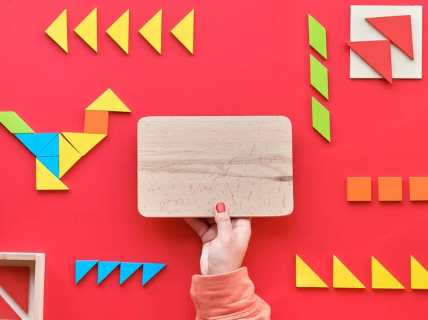 Creative design for Autism World Day on April 2. Tangram elements scattered and arranged in pictogram on red background. Hand hold wooden board with text space, copy-space.