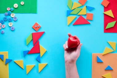 Eller kırmızı taş kalbi tutuyor. 2 Nisan Dünya Otizm Farkındalık Günü için yaratıcı tasarım. Tangram üçgenleri, bulmaca elementleri. Düz yatış, üst görünüm, soyut geometrik yaratıcı arkaplan. Kalbi tut..