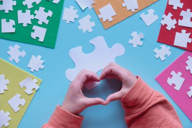 Eller kalp işaretini gösteriyor. Yaratıcı düzenleme üzerine düz bir bakış açısı. Yapboz elementleri ve mavi arkaplanda çok renkli keçeli çarşaflar.