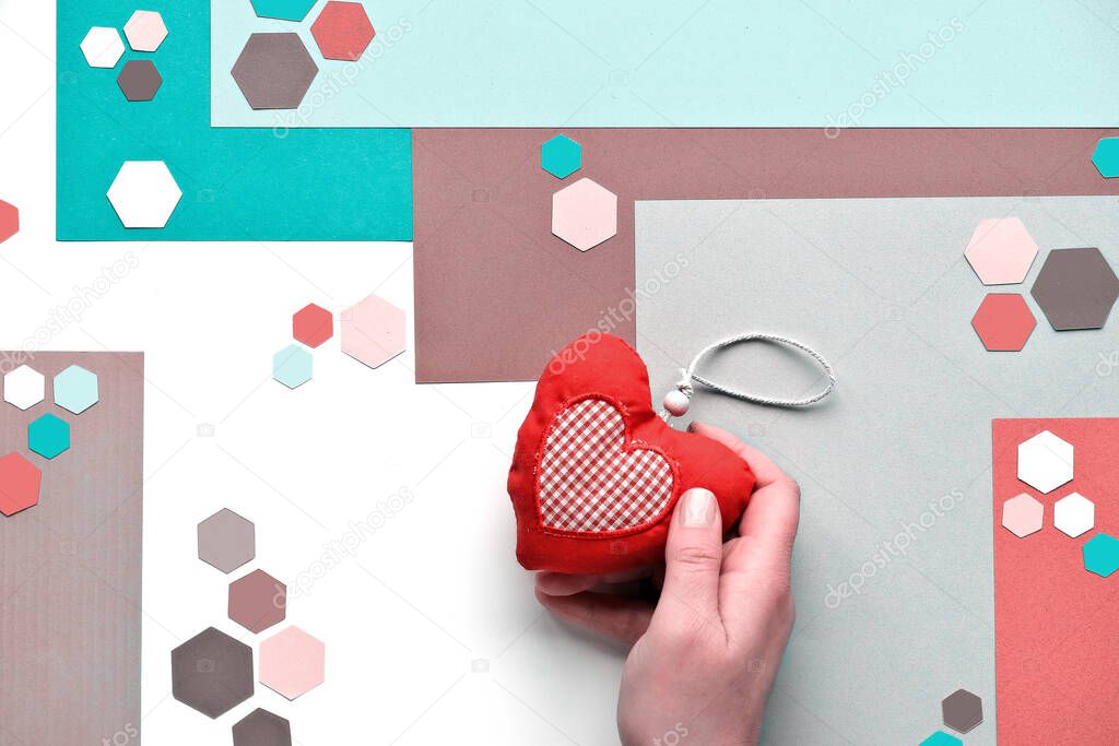 Handmade soft toy heart. Abstract geometric layered paper background with trendy hexagons in neutral muted colors, mint green, red and brown. Flat lay, top view on white background.