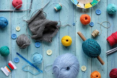 Decorative frame made of wool bundles, yarn balls, buttons and cord. Latch and knitting needles. Creative flat lay on light mint blue wood.