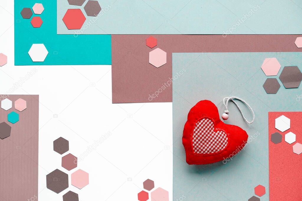 Handmade soft toy heart. Abstract geometric layered paper background with trendy hexagons in neutral muted colors, mint green, cyan, red and brown. Flat lay, top view on white background.