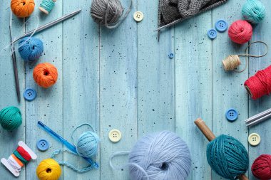 Decorative frame made of wool bundles, yarn balls, buttons and cord. Latch and knitting needles. Creative flat lay on light mint blue wood with copy-space, place for your text.