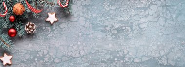 Kopya uzayı olan Xmas panoramik afişi. Noel ağacı dalları, kurdeleler, koniler, baston şekerler ve yün eldivenler. Yaratıcı düz, koyu dokulu arkaplanda yatıyordu.