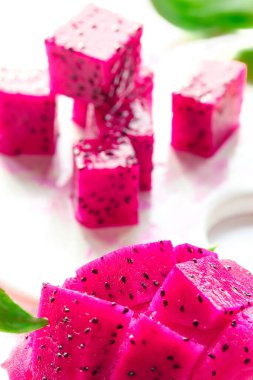 Pembe ejderha meyvesi, pitaya veya pitahaya beyaz tabakta küp şeklinde kesilmiş. Moda süper yiyecek malzemesi. Dilimlere yakın çekim, beyaz tabakta meyve küpleri..