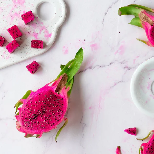 Ugly food. Juicy pink dragon fruit, pitaya, pitahaya sliced on marble table. Trendy top view, swuare composition, flat lay of dragonfruit pieces and shavings.