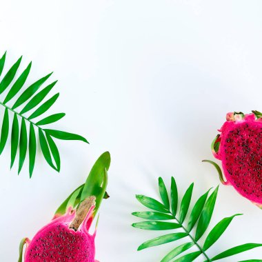 Fresh organic pink dragon fruit, pitaya or pitahaya with pink middle. Trendy top view with palm leaves on white background with text space.