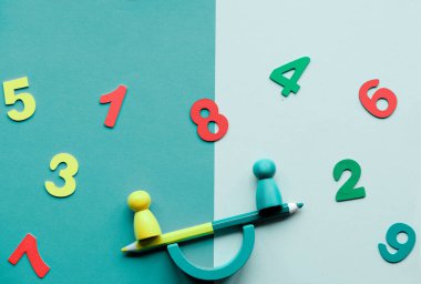 Two figures on a swing, seesaw, on two tone green grey paper. Numbers from one to ten. Concept image for Early Signs of Learning Disabilities in Preschool and Kindergarten.
