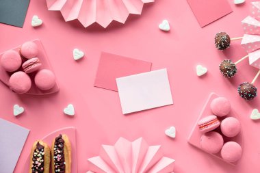 İçinde cspace olan davetiye kartları. Renkli şekerli kremayla süslenmiş çikolatalı pasta. Pembe kağıt üzerinde katlanmış kağıt yelpaze, konfeti, şeker kalpli, pipetli yaratıcı tek renkli üst görünüm