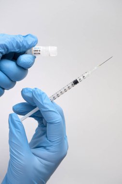 Coronavirus Sars-CoV-2 tarafından üretilen Covid-19 aşısı. Ellerinde şırınga ve aşı şişesi tutan cyan nitril eldivenler var. Tarafsız gri arkaplana yakın çekim.