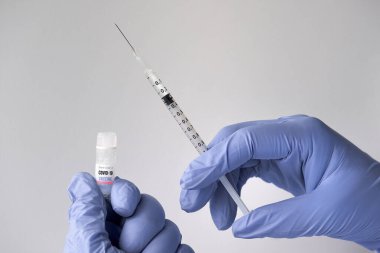 Coronavirus Sars-CoV-2 tarafından üretilen Covid-19 aşısı. Ellerinde şırınga ve aşı şişesi olan eldivenler..