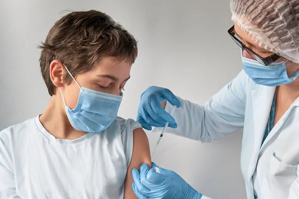 Coronavirus, flu or measles vaccine concept. Medic, doctor or nurse with vaccine vial and syringe. Mature European female tech in face mask, glasses, disposable hat, gloves and protective white gown.