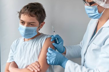 Coronavirus, grip ya da kızamık aşısı konsepti. Sıhhiye, doktor, hemşire, üniforma giyen sağlık görevlisi, mavi eldiven ve maske takan genç çocuğu şırıngayla aşıladı..