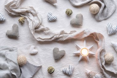 Keten arka planda el yapımı keten kalpler ve toplar. Tarafsız renklerde tekstil el işi. Yumuşak kalbi tut. Monokromatik görünüm. Çay lambasıyla taşralı mevsimlik dekor.