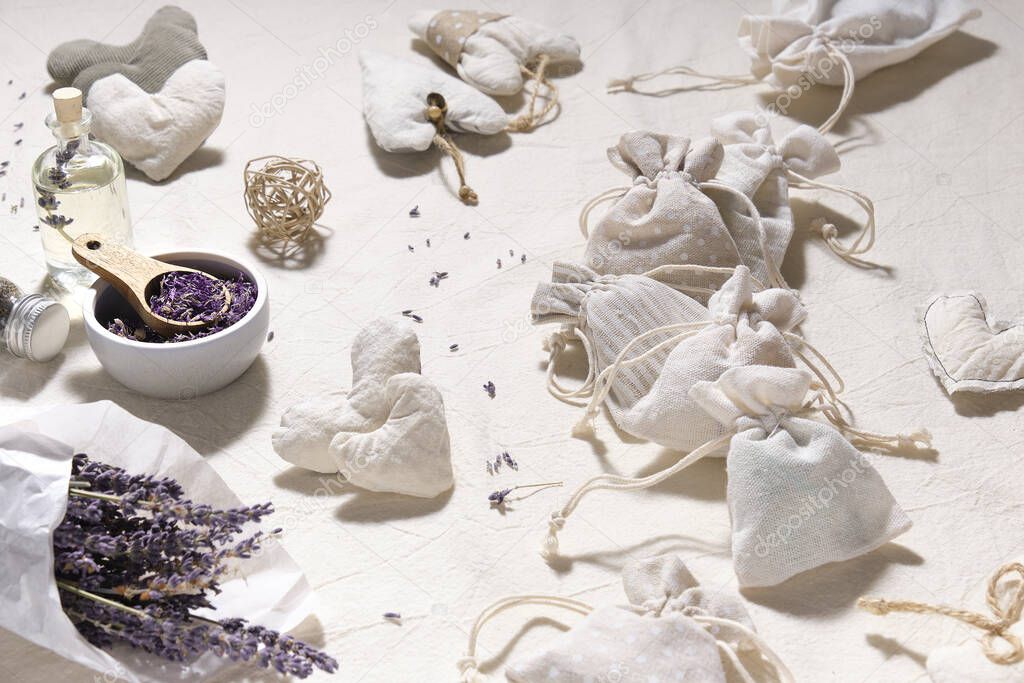 Hand made lavender sachets in textile bags and cotton hearts on cotton tablecloth. Dry lavender flowers in tracing paper and lavender oil. Natural homemade gifts. Zero waste lifestyle.