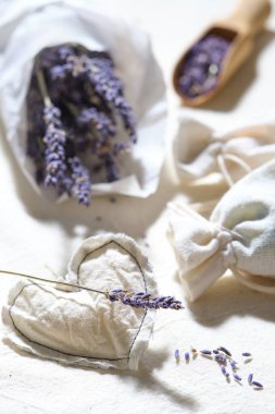 Kuru lavanta çiçeklerine yakın plan beyaz iz kâğıdı. Beyaz pamuk masa örtüsü üzerinde el yapımı lavanta kesesi. Düşük etkili rustik dekorasyon. Kuru lavanta çiçekleri ile ahşap kepçe. Lavanta yağı.