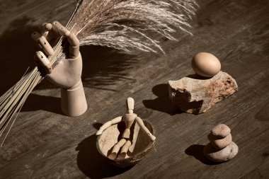 Tahta model el, kuru otları tutuyor. Hindistan cevizi kabuğundan bir insan figürü. Gerçeküstü dekorasyonlar, zen taşı kuleler. Antika, retro grange. Koyu ahşap üzerinde hayat, tek renkli sepia tonlama..