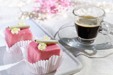 Badem ezmesi ve krema çiçekli sevgililer günü kurabiyeleri. Cam bardakta Espresso kahvesi. Beyaz tekstil masa örtüsünün üzerindeki ışık çelenkleri. Pembe sümbül çiçeği. Sevgililer günün kutlu olsun. 