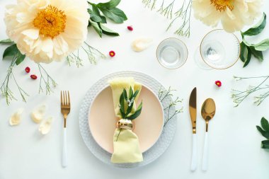 Zahmetsiz bir doğum günü yemeği masası dekoru. Soluk sarı şakayık çiçekleri ve Geç Bahar, Yaz düzlüğü. Beyaz yemek masası, beyaz ve altın kaplar, çiçekler ve yeşilliklerle süslenmiş..