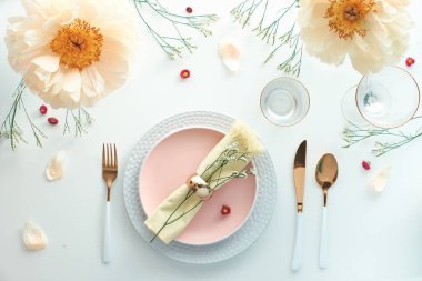 Zahmetsiz bir doğum günü yemeği masası dekoru. Soluk sarı şakayık çiçekleri ve Geç Bahar, Yaz düzlüğü. Beyaz yemek masası, beyaz ve altın kaplar, çiçekler ve yeşilliklerle süslenmiş..