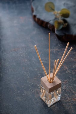 Bambu çubuklu oda parfümü yayıcı ve cam parfüm şişesi. Dekoratif okaliptüs yaprakları, taş. Eskimiş arka planda dekoratif tepsi. Retro stili zarif aromaterapi konsepti.