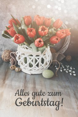 Text Alles gute zum Geburtstag means Happy Birthday in German. Bunch of red flowers in wattle rattan wooden vase on rustic wooden table with pussy willow twigs. Spring birthday greeting card design.