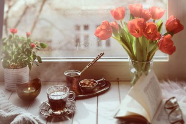 Geleneksel Türk bakır kahve makinesinde pişirilmiş doğu kahvesi. Pencere kenarında çiçekler. Bir sürü lale ve eski kitapla dolu ahşap pencere pervazı. Baharda soğuk yağmurlu bir gün. Samimi sahne, higge konsepti.