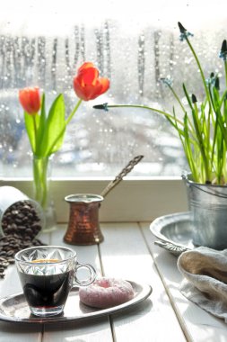 Geleneksel bakır kahve demliğinde, pencere pervazında çiçekler olan doğu kahvesi. Turuncu laleli ahşap pencere pervazı ve sümbül saksısı. Baharda soğuk yağmurlu bir gün. Samimi sahne, higge konsepti.