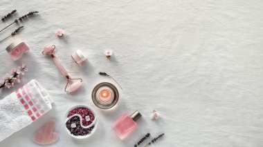 Kristal gül kuvars yüz silindiri, yüz masajı için Gua sha taşı. Beyaz tekstil ürünlerinden uzak dur. El yapımı aromatik tuz, kuru lavanta. Temel yağ, bakım ürünleri. Panoramik resim, kopyalama alanı.