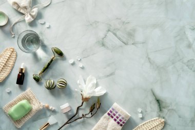 Güzellik masajı için yeşim yüz silindiri, cilt bakımı ürünleri. Gerekli yağ şişesi. Beyaz mermer masanın üzerinde yatıyordu. Manolya çiçekleri, yeşil nesneler. Üst görünüm, kopyalama alanı, metin yeri.