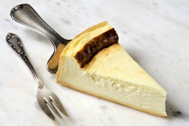 Klasik kek sunucusunda beyaz tabakta peynirli kek dilimi ve mermer tabakta pasta çatalı. Geleneksel Alman tatlısı.