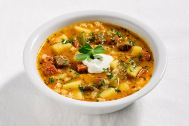 Rassolnik, biftek, arpa, havuç ve turşu çorbası. Tuzlu-ekşi salatalıkla pişirilmiş. Beyaz tekstil masa örtüsü üzerine beyaz kâse içinde çorba. Ekşi krema ve maydanozla servis edilir..