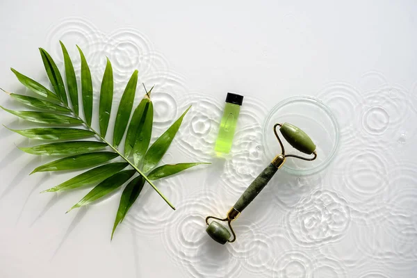 Green liquid product for beauty facial massage therapy, Self made skincare product. Top view, simple composition, palm leaf on white. Water rings, shadows of ripple circles.