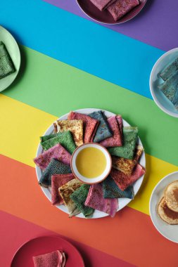 Gökkuşağı krepleri, farklı renkte krepler. Ispanak, pancar tozu, mavi kibrit ve zerdeçal krepleri. Renkli gözlemeler, gökkuşağı renkli kağıdın üzerinde düz uzanmış..