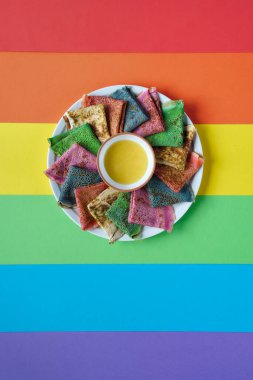 Gökkuşağı krepleri, farklı renkte krepler. Ispanak, pancar tozu, mavi kibrit ve zerdeçal krepleri. Renkli krepler, gökkuşağı renkli kağıdın üzerinde düz uzanmış. Kopyalama alanı, metin için yer.