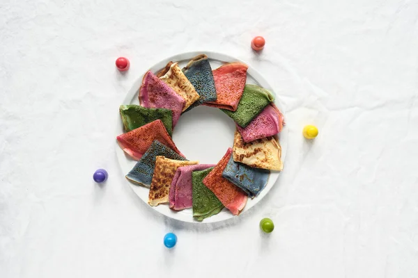 Rainbow party, table setup. Vibrant crepes on place. Off white textile cotton tablecloth. Wooden figurnes and Rainbow as symbol of compassion, friendship and inclusivity, LGBT pride.